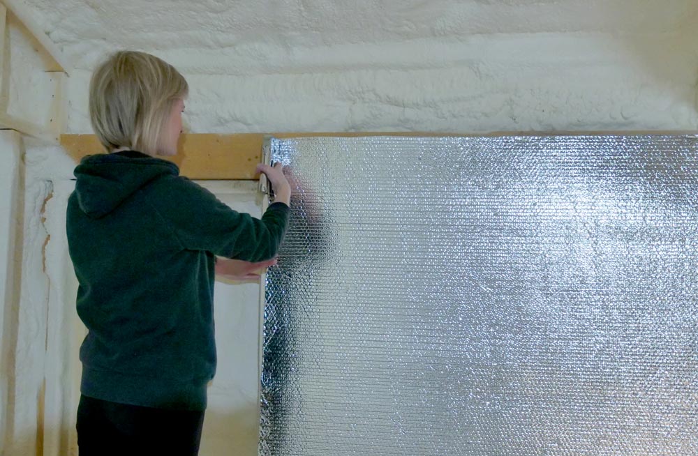 person stapling reflective insulation along a wall